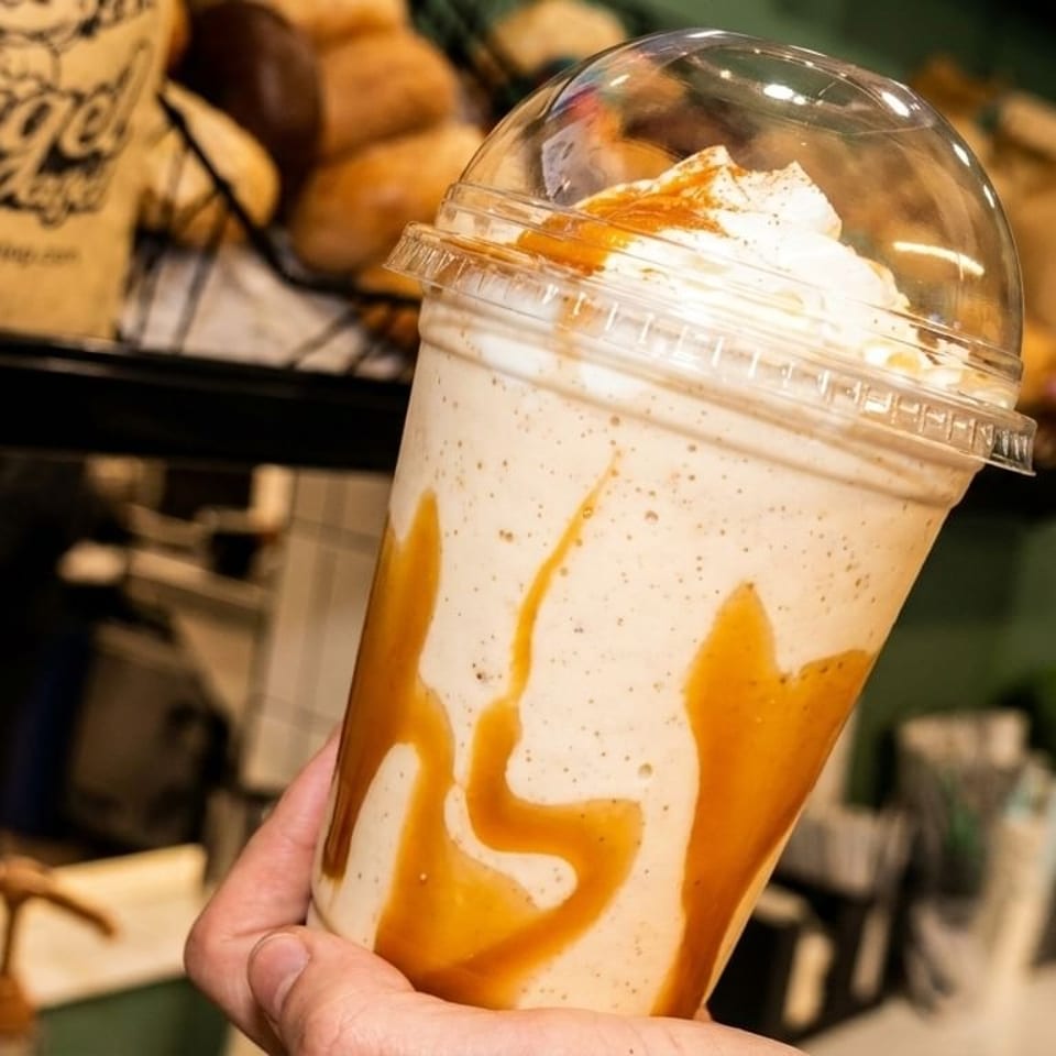 Hand holding a caramel-swirled milkshake with whipped cream and a clear dome lid.