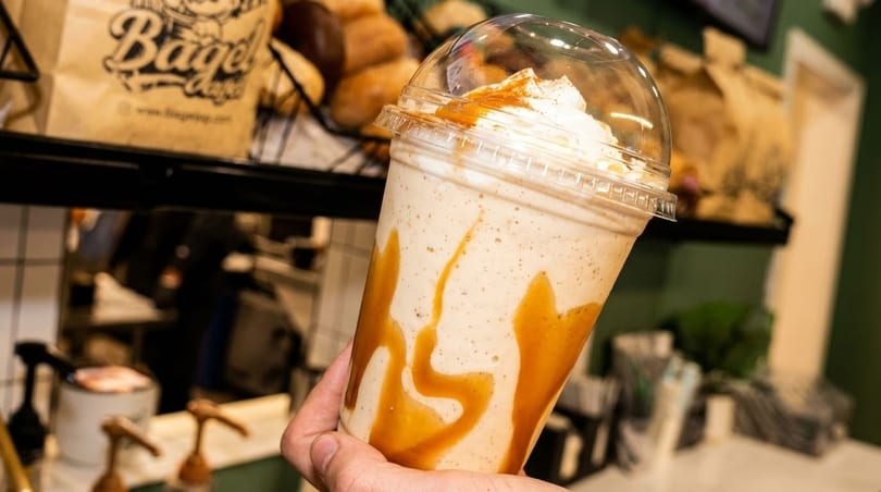 Hand holding a caramel-swirled milkshake with whipped cream and a clear dome lid.
